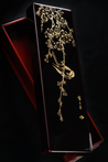A black watch box with a bird perched on a branch in gold and a red interior 